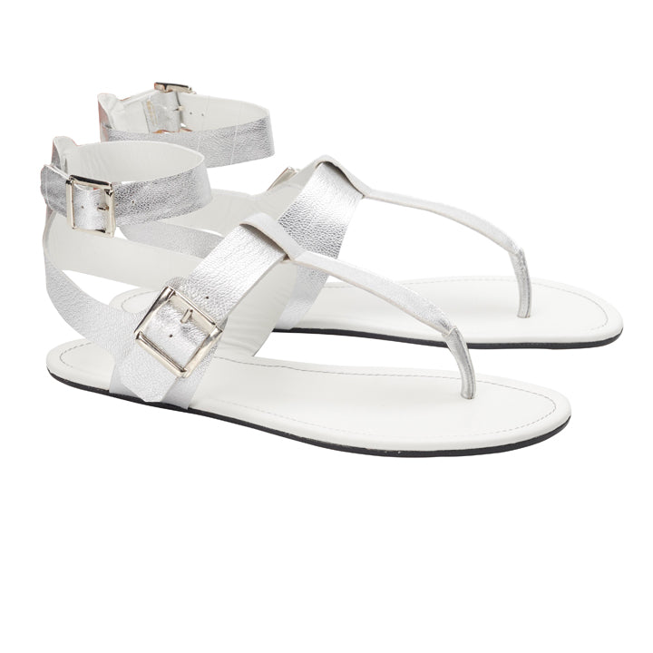 Wir präsentieren das QAPRI Silver von ZAQQ: ein Paar flache silberne Sandalen aus Nappaleder. Diese Barfußsandalen verfügen über Knöchelriemen mit Schnallen und ein minimalistisches Design im Zehentrenner-Stil, das elegante, moderne Ästhetik mit außergewöhnlichem Komfort verbindet.