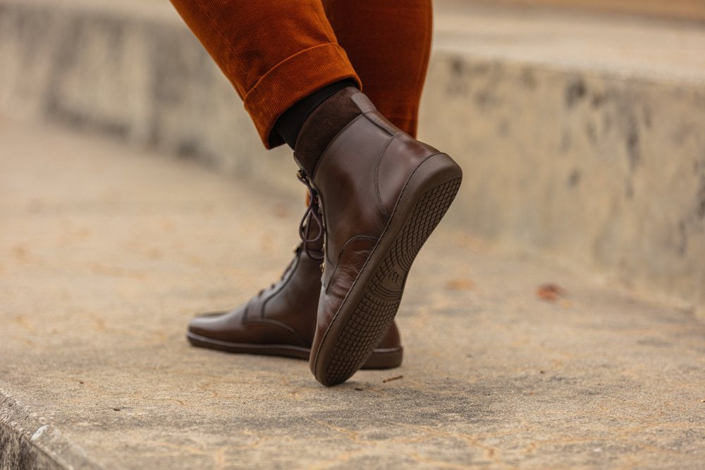 Eine Person in braunen Stiefeletten von QORBY und rostfarbenen Hosen geht Betonstufen hinauf. Die Stiefel bieten eine ideale Mischung aus Stil und dem für ZAQQ typischen Tragekomfort.