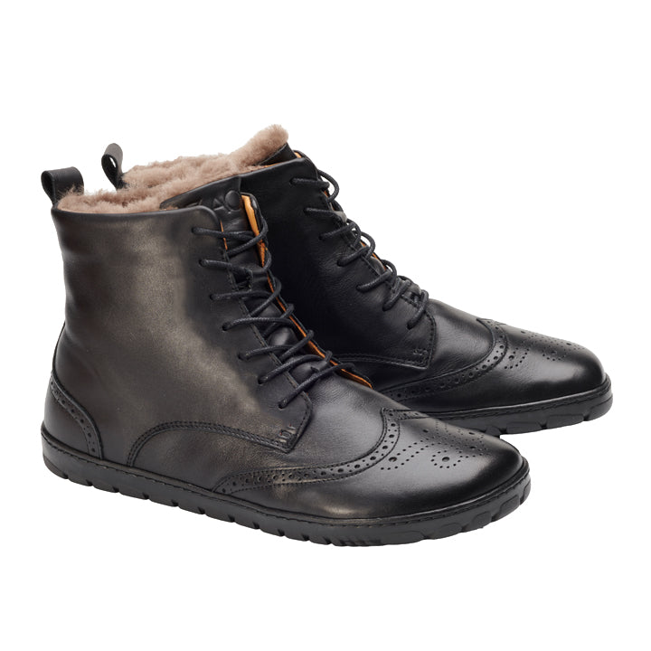 Ein Paar QUINTIC Winter Brogue Black-Stiefel von ZAQQ aus Nappaleder mit Brogue-Stil-Details und Fellfutter, aus einer Schrägansicht. Diese Winterstiefel haben schwarze Schnürsenkel und eine praktische Schlaufe an der Rückseite zum einfachen Tragen, vor einem strahlend weißen Hintergrund.