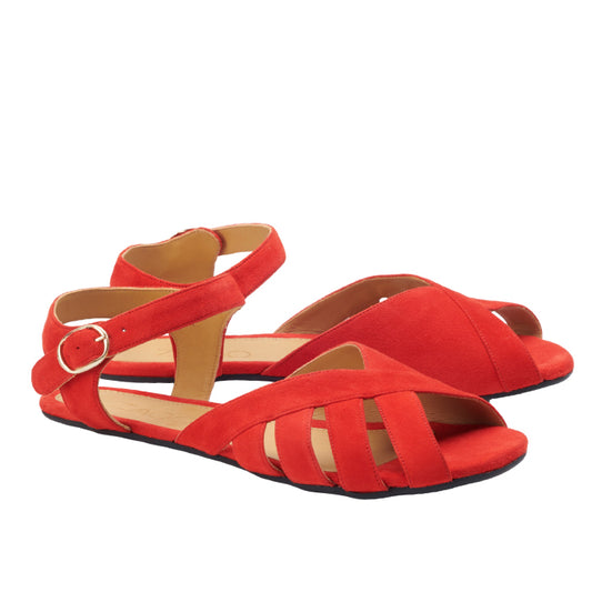 Die roten Sandalen QORSE Red von ZAQQ aus Veloursleder haben überkreuzte Riemen und eine Knöchelschnalle. Auf weißem Hintergrund präsentiert sich das Design mit offener Spitze und flacher Sohle und sorgt für einen lässigen und doch stilvollen Look, der an Barfußschuhe erinnert.