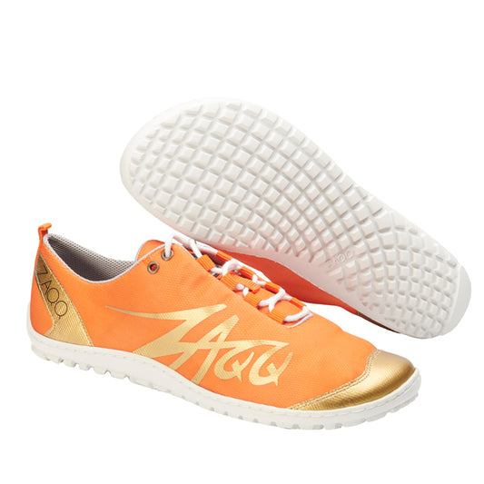 Wir präsentieren die SQIM Orange Gold Sportschuhe von ZAQQ: ein lebhaftes Paar aus recycelten Materialien, mit auffälligen Orangetönen und weißen Sohlen. Das Design wird durch einen goldenen Streifen und eine Zehenkappe akzentuiert, ergänzt durch weiße Schnürsenkel und das Logo der Marke an der Seite. Gefeiert für ihren Tragekomfort, ist ein Schuh auf der Seite liegend abgebildet, während der andere aufrecht steht.