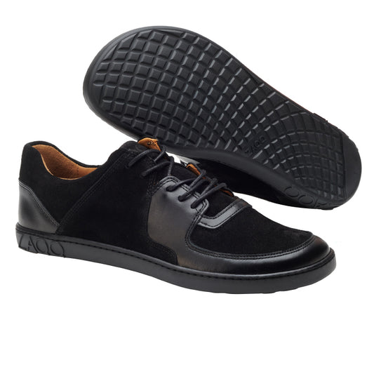 Wir präsentieren den IVIQ Black von ZAQQ: ein anspruchsvolles Paar Schuhe mit elegantem Design, fachmännisch gefertigt aus hochwertigem Leder und schwarzem Veloursleder. Ein Schuh steht aufrecht, während der andere seine Sohle zeigt, die mit einem gitterartigen Muster für Halt gestaltet ist, um ein barfußähnliches Laufgefühl zu vermitteln.