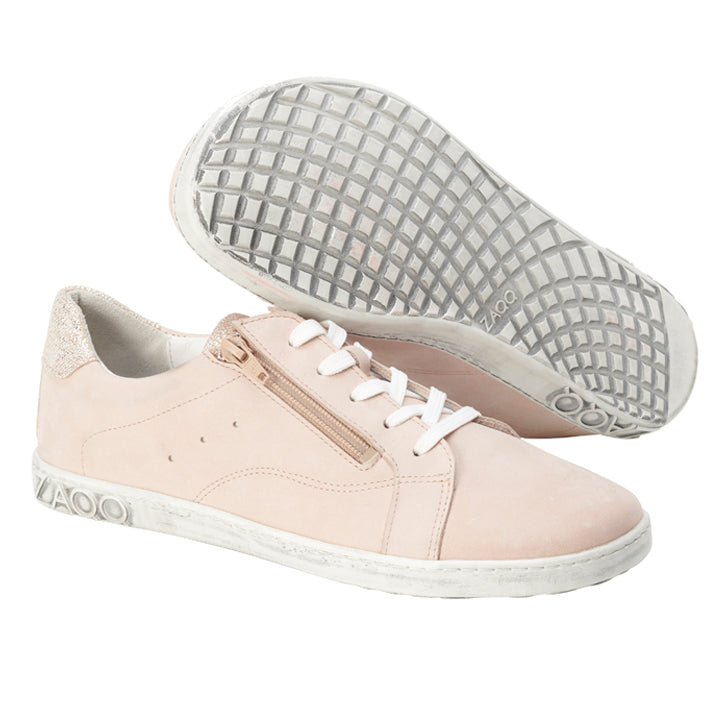 Wir präsentieren den QOMFY Wide Rosa von ZAQQ: elegante hellrosa Sneaker aus hochwertigem Nappaleder. Sie verfügen über weiße Sohlen und Schnürsenkel, wobei ein Sneaker aufrecht steht und einen seitlichen Reißverschluss und eine strukturierte Ferse aufweist. Der andere Sneaker ist geneigt, um seine Sohle mit Gittermuster zu präsentieren und hebt stolz das ZAQQ-Branding sowohl an der Ferse als auch an der Sohle hervor.