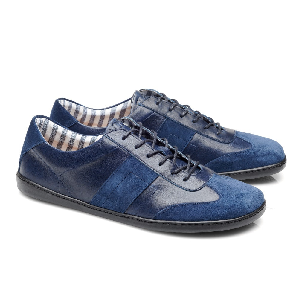 Die TORQUAY Blue Sneaker von ZAQQ sind aus blauem Leder mit Wildlederakzenten gefertigt, hervorgehoben durch dunkle Schnürsenkel und schwarze Sohlen. Die Innenseite zeigt ein Streifenmuster in Braun- und Weißtönen, komplett mit einem weichen Baumwollinnenfutter.