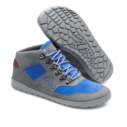 Wir präsentieren die wasserdichten HIQE Mid Azure-Schuhe von ZAQQ: ein stilvolles Paar Freizeitschuhe mit grauen und blauen Einsätzen, auffälligen blauen Schnürsenkeln und braunen Akzenten an der Ferse. Diese Schuhe sind aus hochwertigem Veloursleder gefertigt und mit einer strukturierten grauen Sohle gestaltet, auf der das ZAQQ-Branding deutlich zu sehen ist. Der rechte Schuh wird aufrecht stehend präsentiert, während der linke auf der Seite liegt.