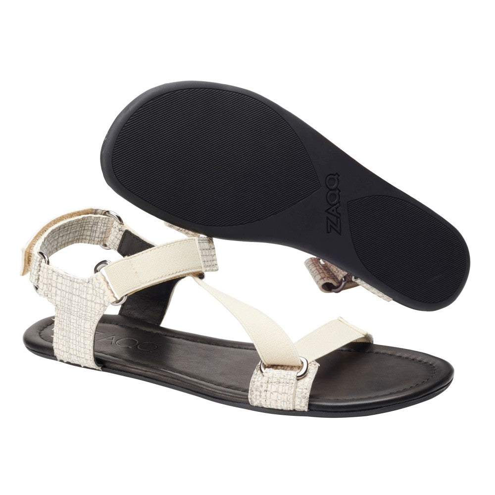 Die MIQA Beige Sandalen von ZAQQ sind aus hochwertigem Veloursleder gefertigt und verfügen über verstellbare Riemen und eine flexible Sohle. Eine Sandale ist von der Seite zu sehen, während die andere ihre Sohle mit einem strukturierten Griffmuster zeigt.