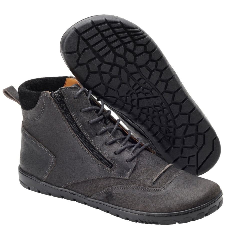 Wir präsentieren die ZAQQ PARQER High-Top-Sneaker in Dunkelgrau. Diese stylischen Schuhe sind aus Veloursleder gefertigt und haben flexible schwarze Sohlen. Ein Schuh wird aufrecht präsentiert, wodurch die seitlichen Reißverschlüsse und Schnürsenkel hervorgehoben werden, während der andere geneigt ist, um sein einzigartiges Profilmuster zu präsentieren.