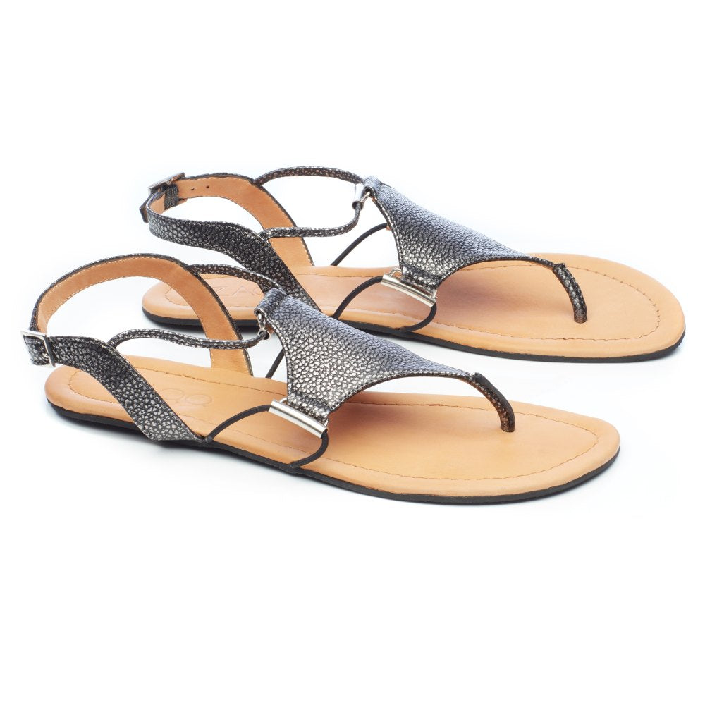 Die QAMINO Black Sandalen von ZAQQ bestechen durch ihre eleganten Riemen aus Nappaleder mit metallischer Textur und die hellbraune Sohle. Diese Barfußsandale mit Zehenschlaufe und Knöchelriemen ist elegant mit kleinen silbernen Akzenten verziert. Vor einem schlichten weißen Hintergrund vereinen sie Eleganz und Komfort.