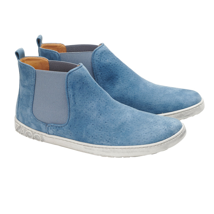 Ein Paar blaue QOLLINS-Chelsea-Stiefel von ZAQQ aus hellblauem Veloursleder und elastischen Seitenteilen mit einer weißen Barfußsohle vor einem schlichten weißen Hintergrund.