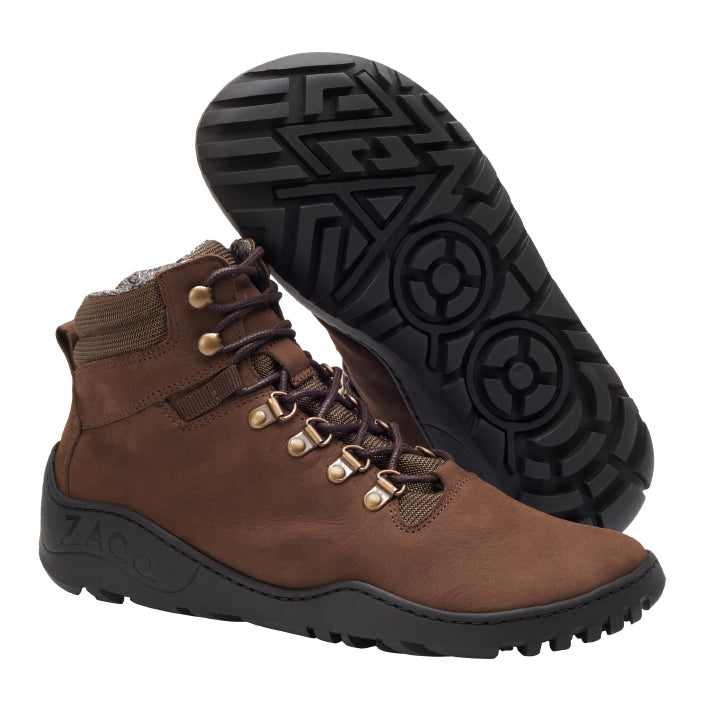 Ein Paar braune ZAQQ MOUNTEQ Waterproof Wanderstiefel mit dunkelbraunen Schnürsenkeln und Metallösen. Die schwarze Sohle hat ein robustes geometrisches Muster mit kreisförmigem Design. Ein Stiefel steht aufrecht, während der andere die Sohle zeigt, was sie ideal für Outdoor-Abenteuer macht.