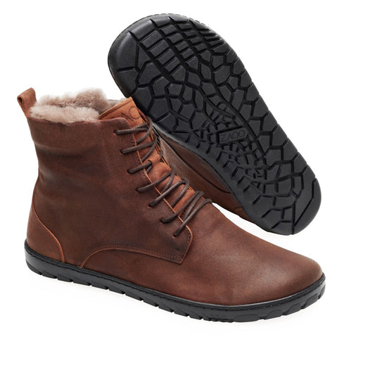 Auf dem Bild sind die ZAQQ QUINTIC Winter Velours Brown Waterproof-Stiefel zu sehen. Ein Stiefel steht aufrecht und hebt sein kuscheliges Lammfellfutter hervor, während der andere das Profilmuster auf seiner schwarzen Sohle zeigt. Diese braunen Lederstiefeletten haben Schnürungen vorne und ein elegantes, minimalistisches Design.