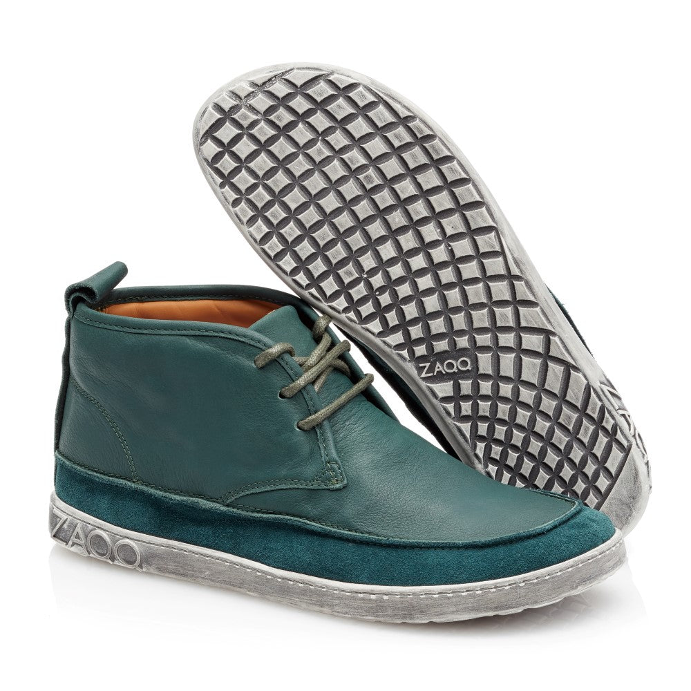 Ein Paar stylische knöchelhohe QUITMAN Green-Sneakers aus Velours- und Glattleder von ZAQQ mit grauer Sohle. Ein Schuh steht aufrecht und zeigt seine Schnürsenkel, während der andere geneigt ist und die Sohle mit Waffelmuster und dem Markennamen ZAQQ zeigt.