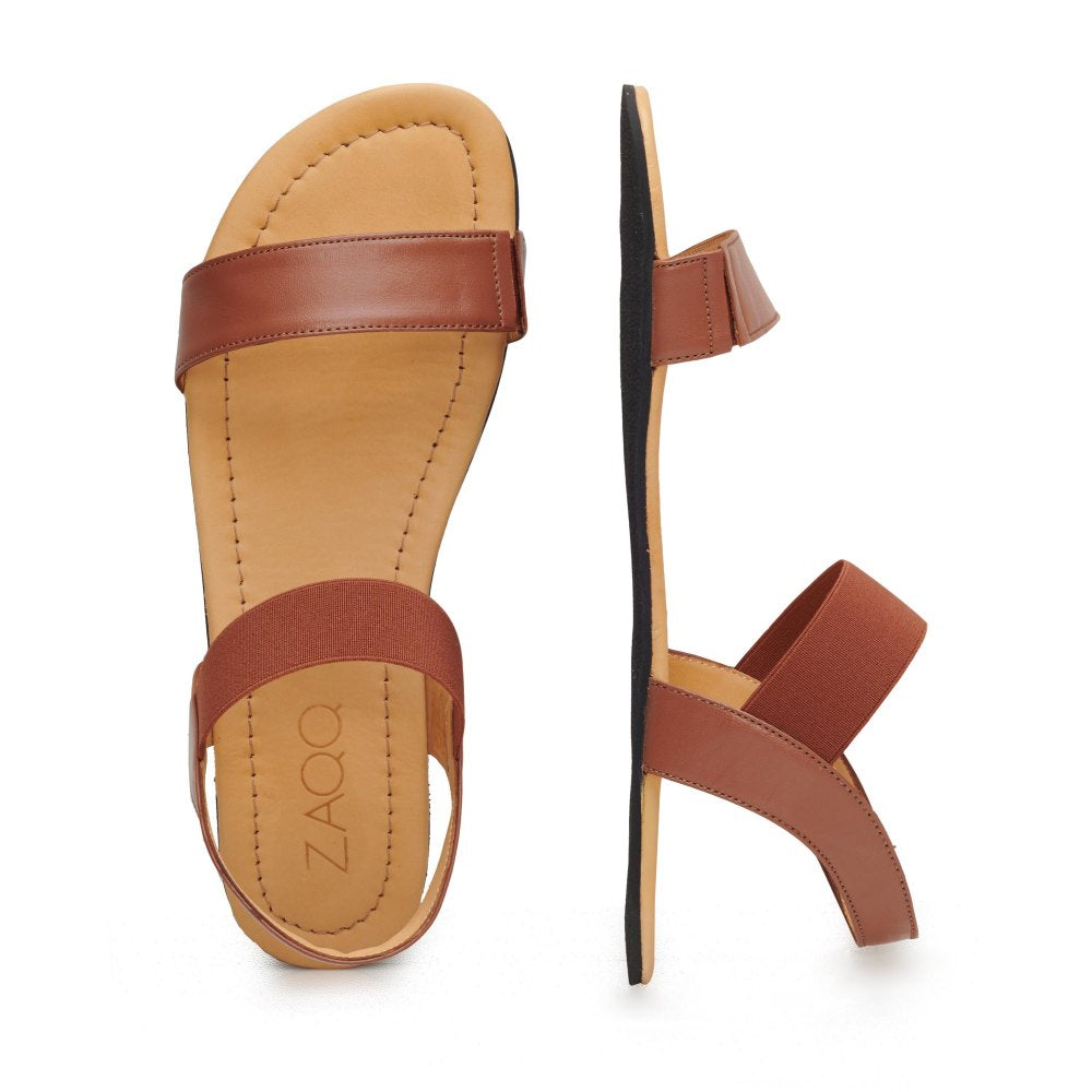 Ein stilvolles und bequemes Paar SLIQ Cognac-Sandalen von ZAQQ zeigt sowohl Mode als auch Komfort. Die linke Sandale ist von oben zu sehen und weist zwei Riemen über dem Fuß auf, während die rechte Sandale von der Seite zu sehen ist und ihre dünne schwarze Sohle und das Riemendesign mit sichtbarem ZAQQ-Branding hervorhebt.