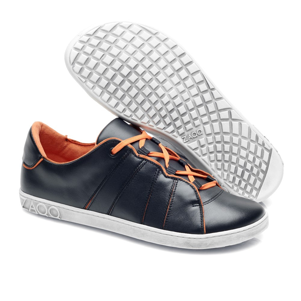 Ein Paar trendige ZAQQ QQQ Low Black Orange Sneaker mit schwarzem Obermaterial aus Leder, leuchtend orangefarbenen Schnürsenkeln und strahlend weißen Sohlen. Ein Sneaker steht aufrecht, während der andere seine gemusterte Sohle zeigt. Das Innere ist mit einem umweltfreundlichen, veganen orangefarbenen Futter versehen.