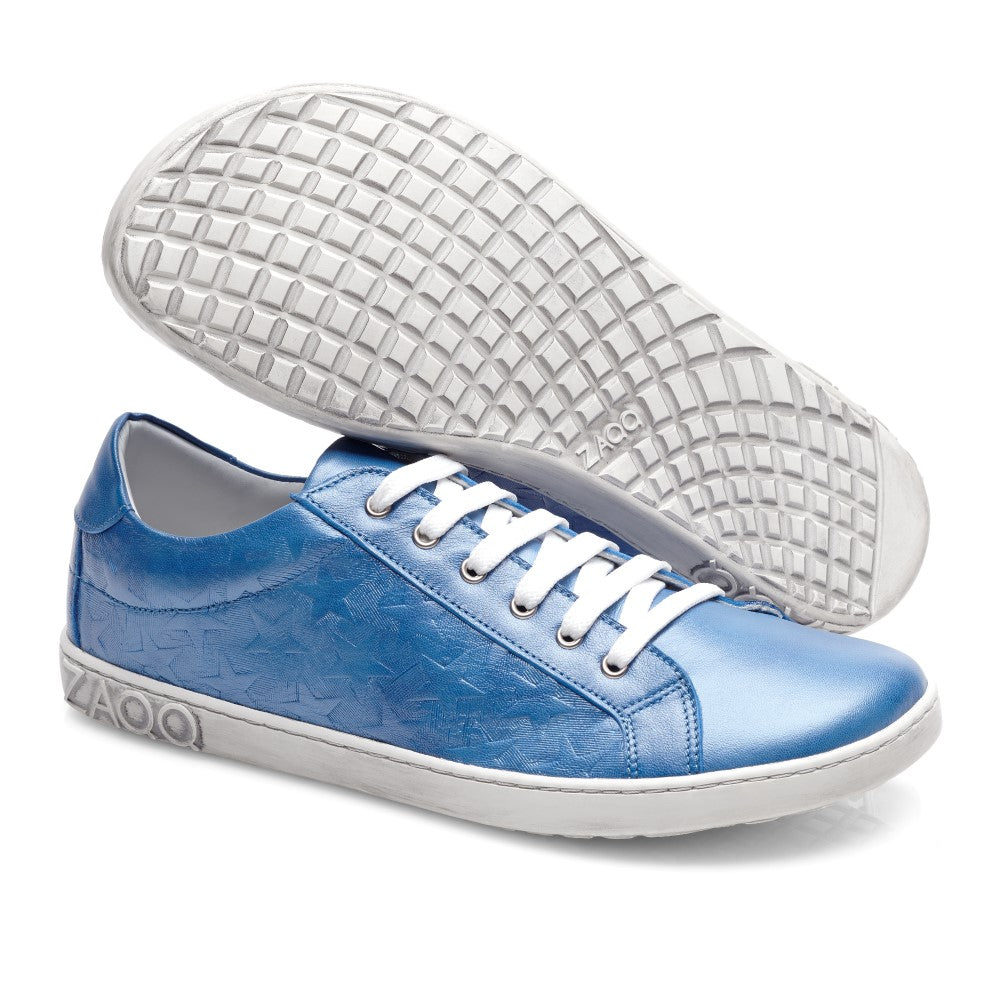 Der SLOQ Stars Blue von ZAQQ ist ein Paar glänzender blauer Sneaker mit Sternenmuster und weißer Sohle. Ein Sneaker steht aufrecht, während der andere auf der Seite liegt, wodurch das aufwendige Profilmuster der Sohlen hervorgehoben wird. Diese Schuhe sind aus glattem Nappaleder gefertigt und mit weißen Schnürsenkeln ausgestattet und vereinen nahtlos Stil und Komfort.