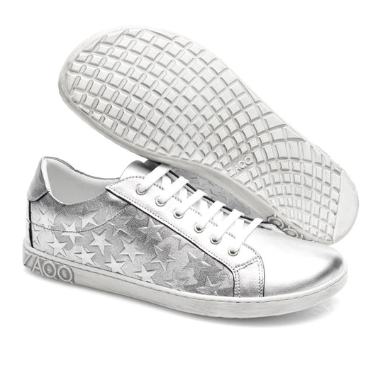 Die SLOQ Stars Silver Sneaker von ZAQQ glänzen mit Sternverzierungen an den Seiten. Diese metallischen Schmuckstücke sind mit weißen Schnürsenkeln und Sohlen ausgestattet, die perfekt abgewinkelt sind, um das detaillierte Profilmuster dieses schicken Sneakers zur Geltung zu bringen.